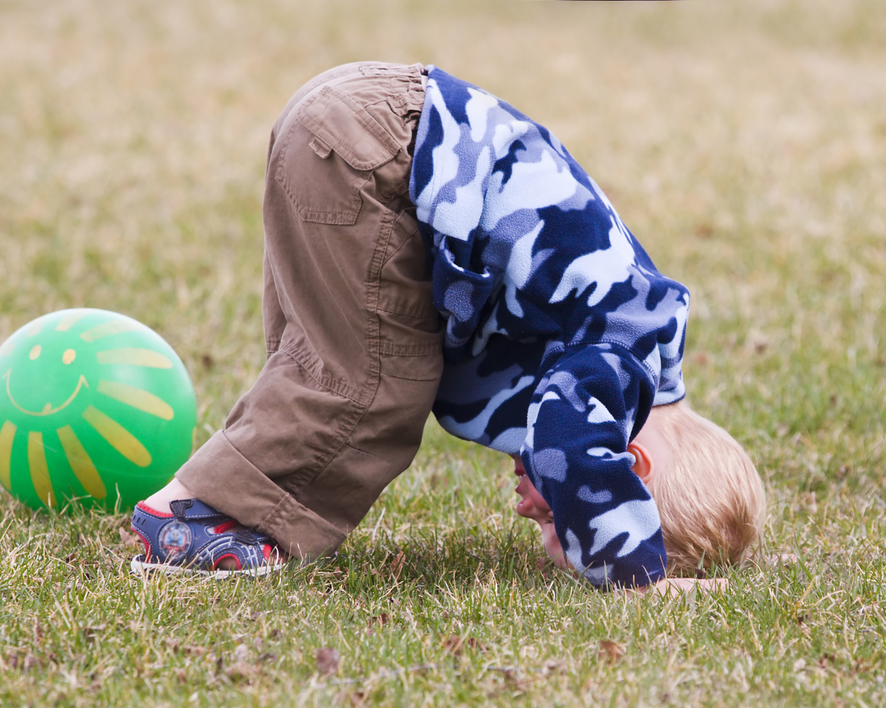Маленький мальчик играет на траве с мячом
