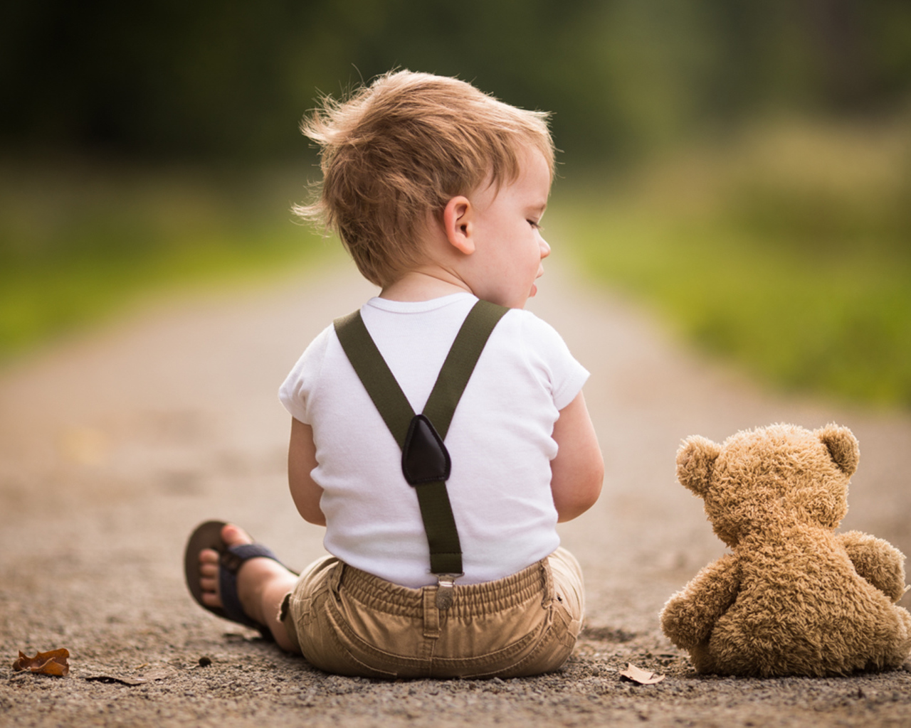 Маленький мальчик сидит на дороге с игрушечным мишкой