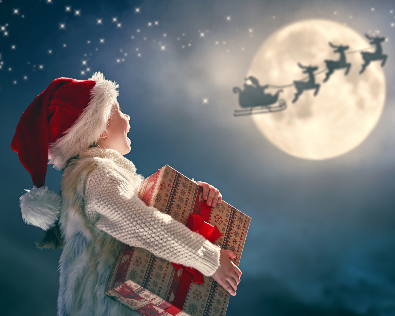 Маленький мальчик с подарком смотрит на улетающего Санта Клауса