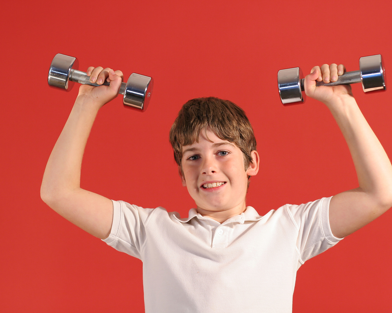 Маленький мальчик с гантелями на красном фоне
