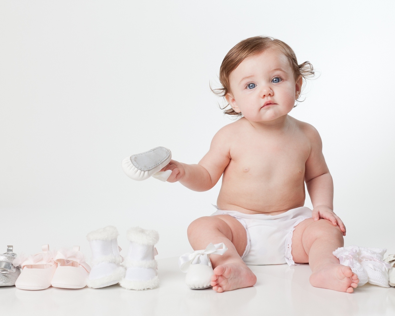 Маленький забавный голубоглазый малыш с обувью на белом фоне
