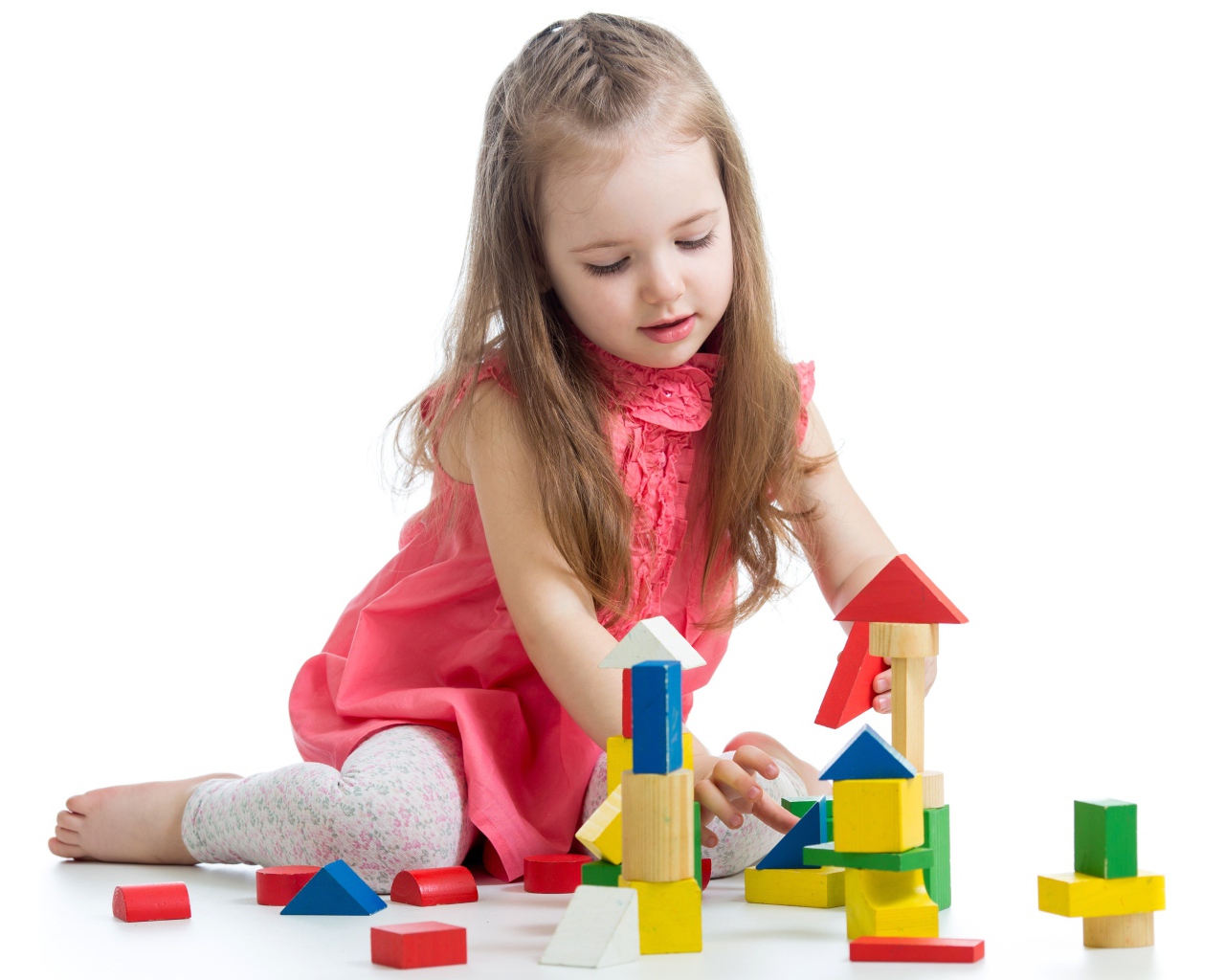 Маленькая девочка строит домик из кубиков на белом фоне