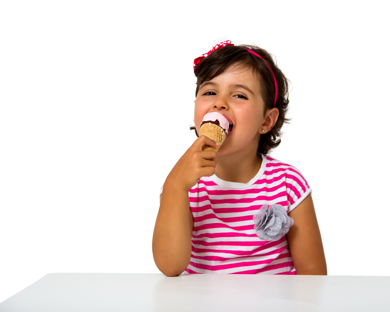 Маленькая девочка ест мороженое за столом на белом фоне