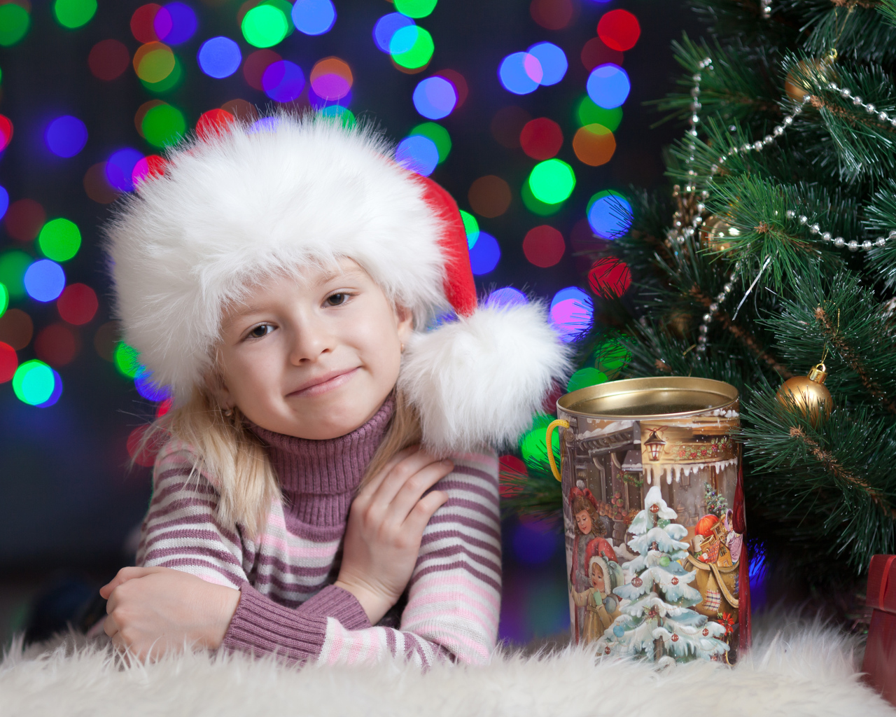 Маленькая девочка в новогодней шапке у елки