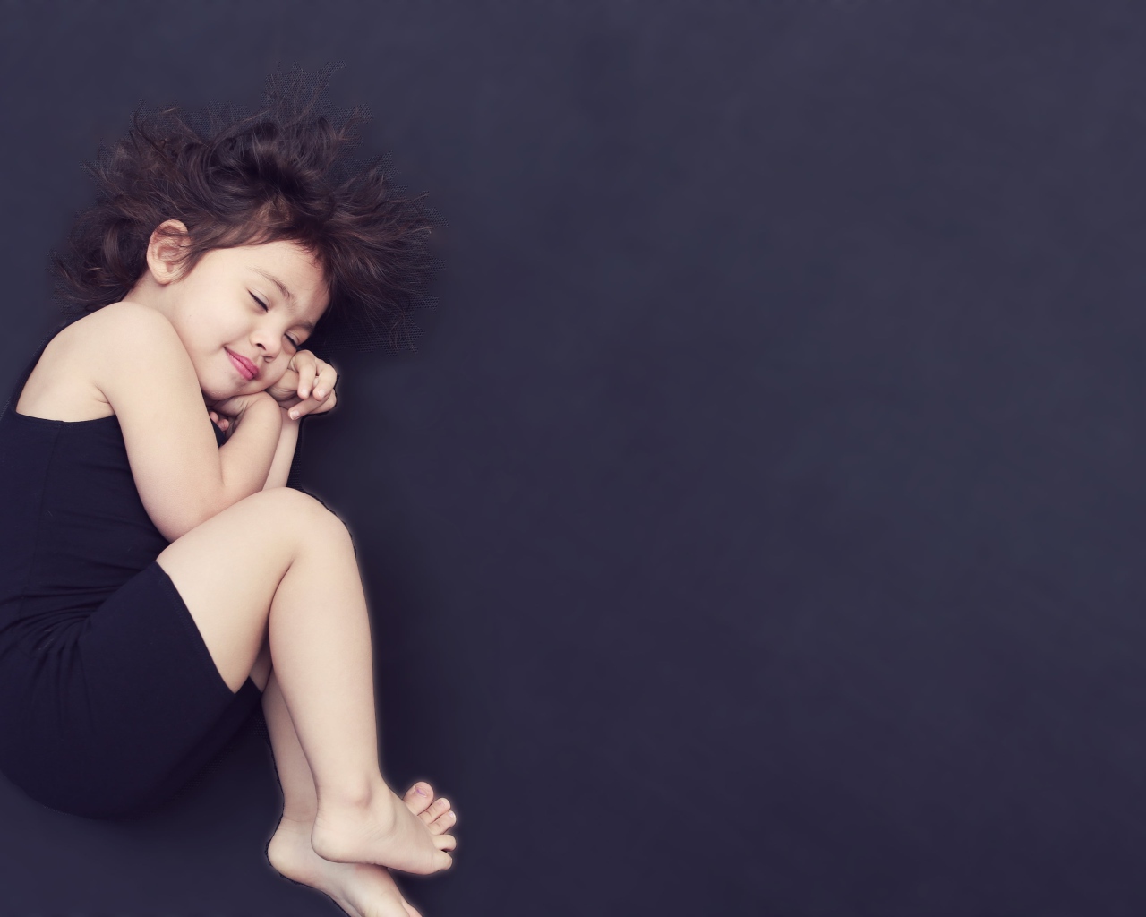 Маленькая девочка в черном платье спит на черном фоне