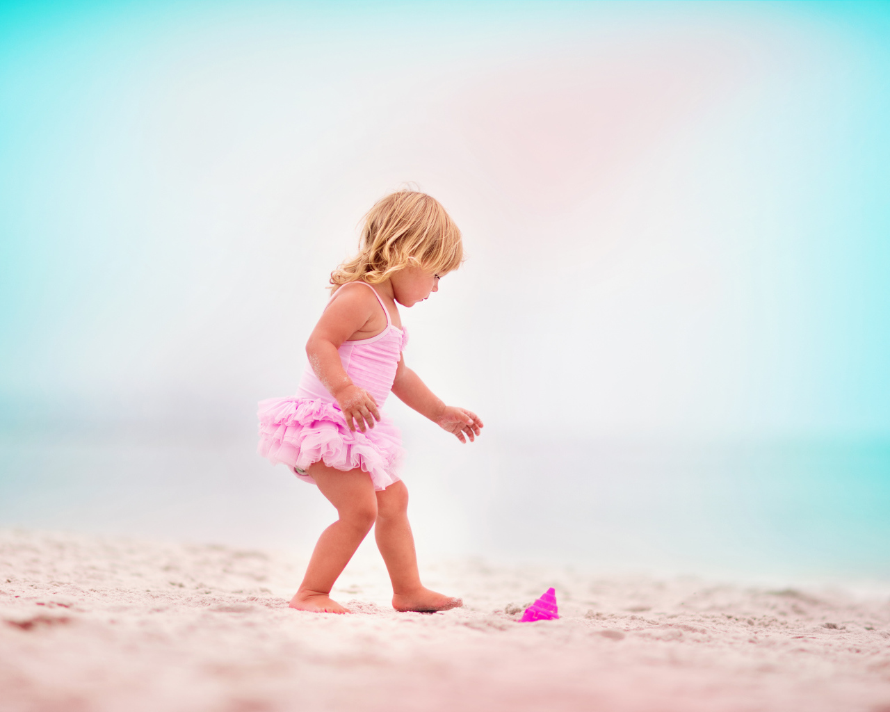 Маленькая девочка в розовом купальнике на песке