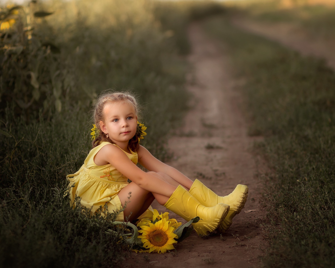 Маленькая девочка в желтом платье сидит на земле с подсолнухами