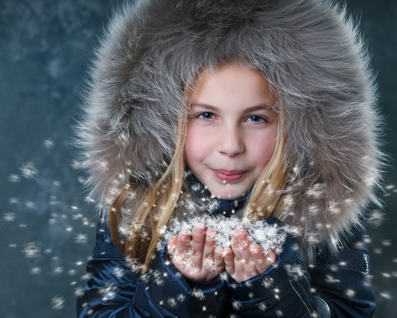 Маленькая девочка в капюшоне сдувает снежинки с ладоней