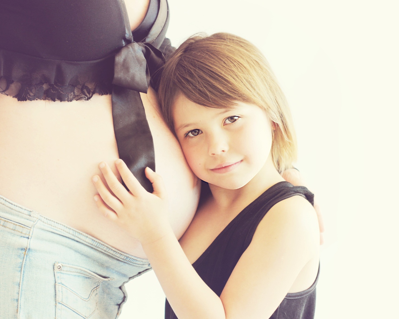 Маленькая девочка прислоняется к животу беременной женщины