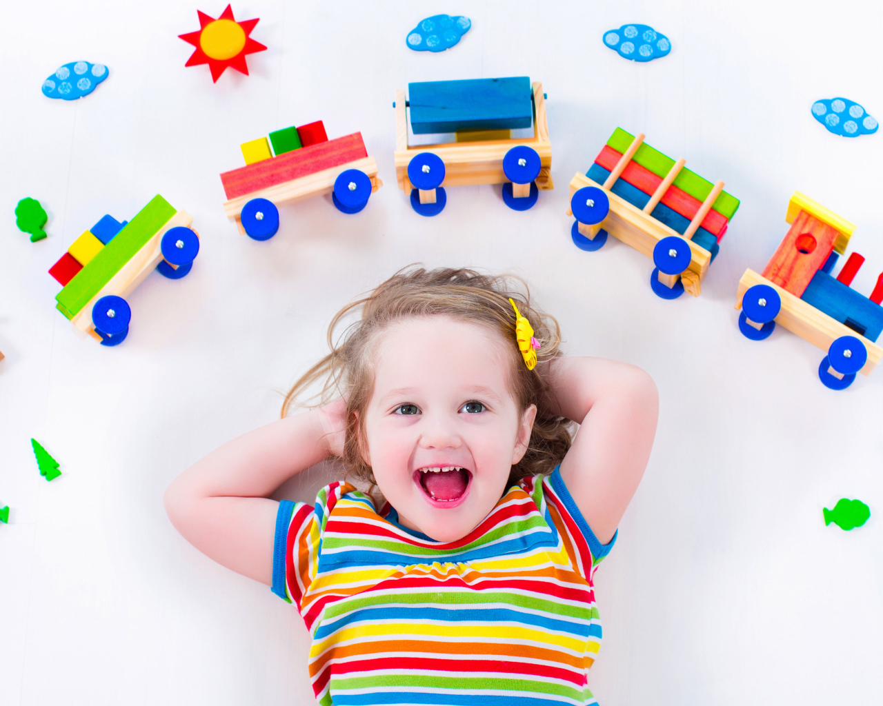 Маленькая девочка на сером фоне с игрушечным паровозом 