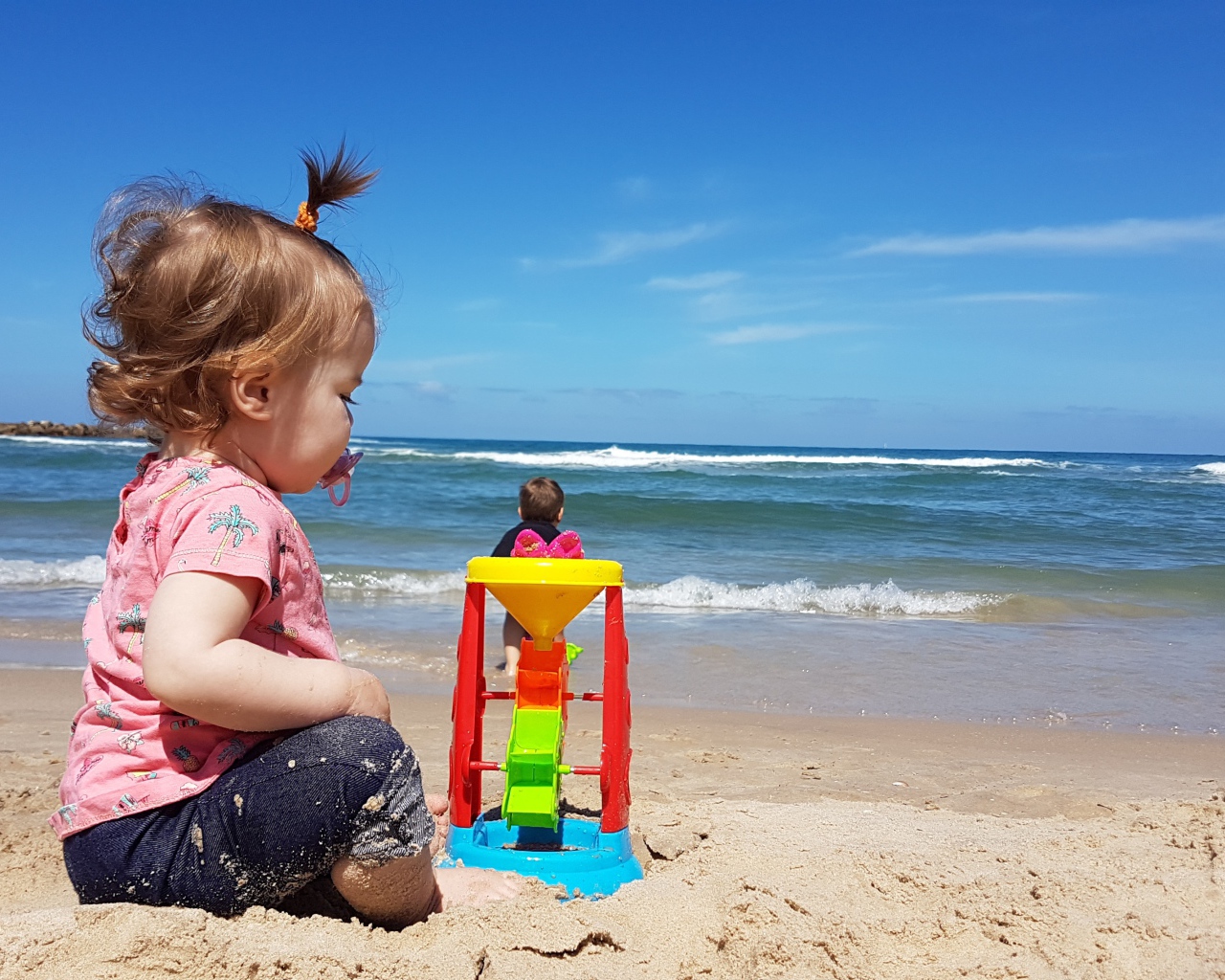 Маленькая девочка играет на песке у моря