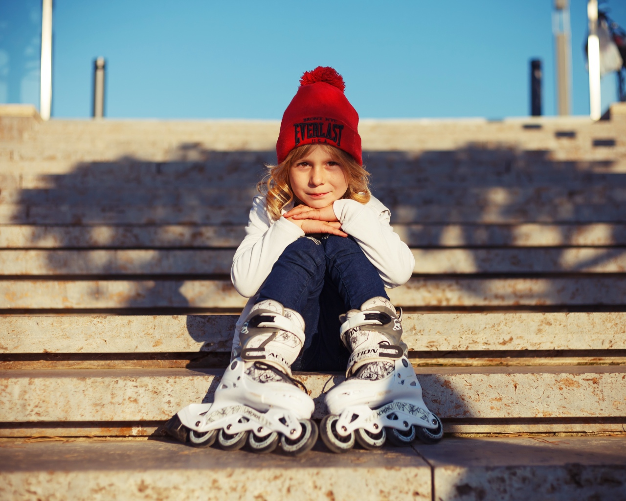 Маленькая девочка в роликах сидит на ступеньках 