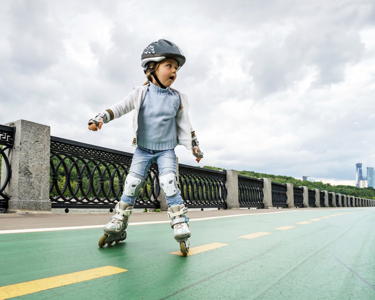 Маленькая девочка катается по мосту на роликах
