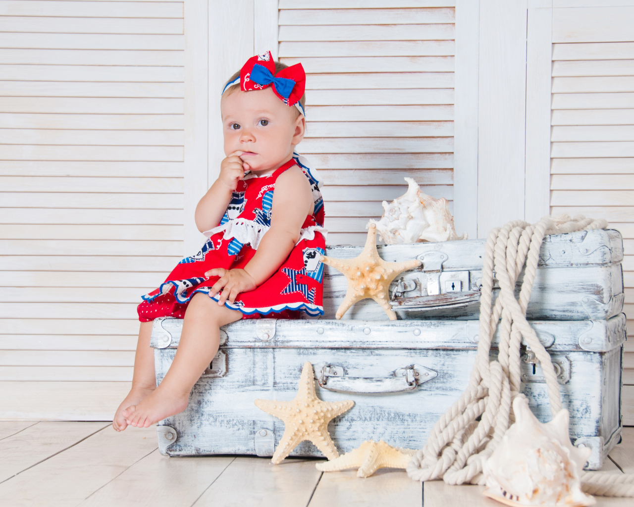 Маленькая девочка сидит на чемодане с морскими звездами