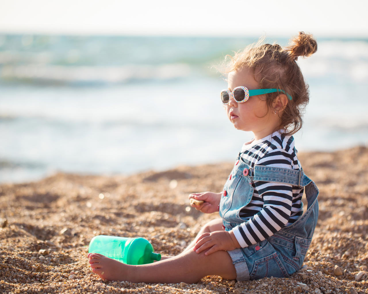 Маленькая девочка сидит на песке на пляже