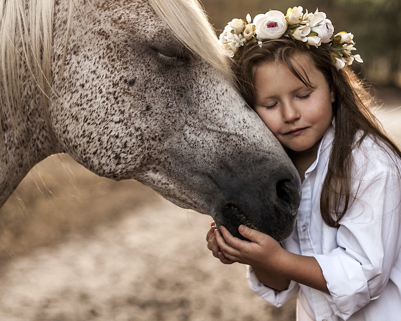 Маленькая девочка с венком на голове обнимает лошадь