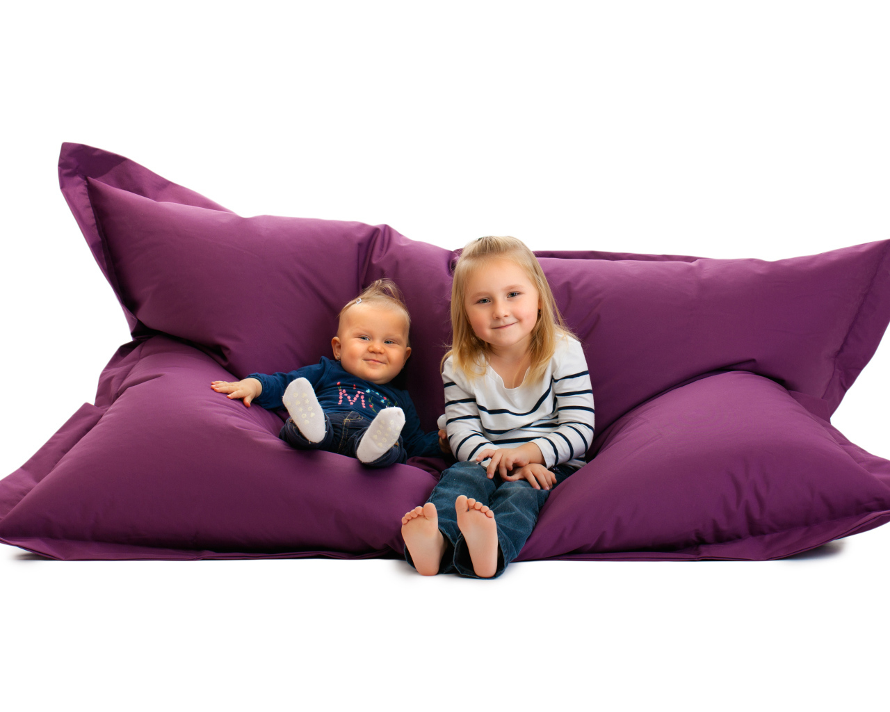 Маленькие девочки сидят на мягкой подушке на белом фоне