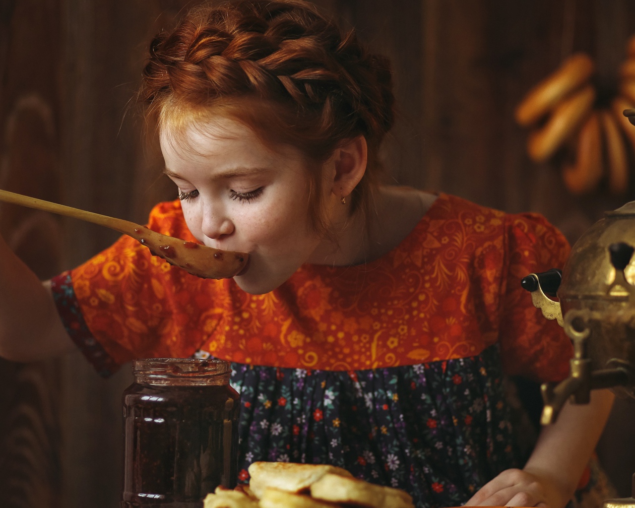 Маленькая рыжеволосая девочка пробует варенье