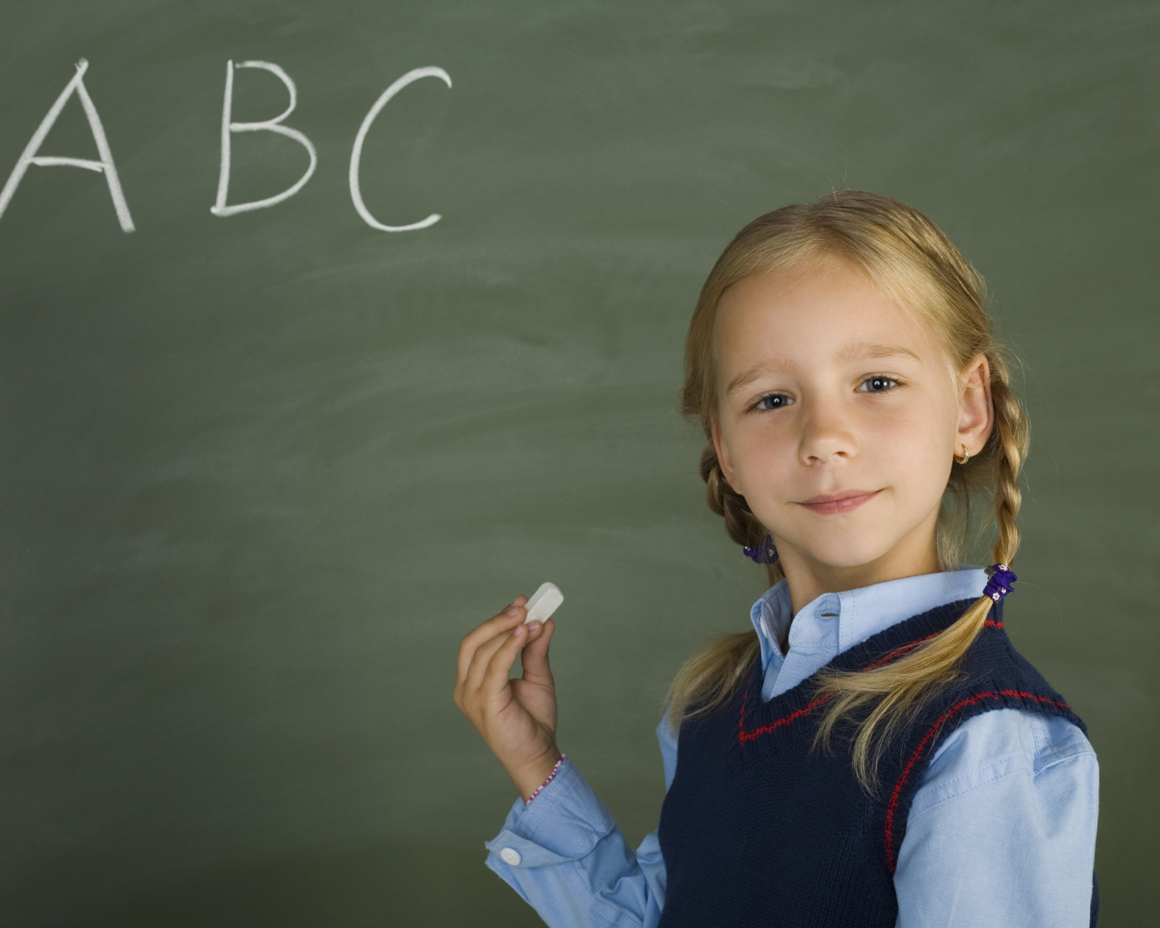 Маленькая школьница пишет буквы на доске 