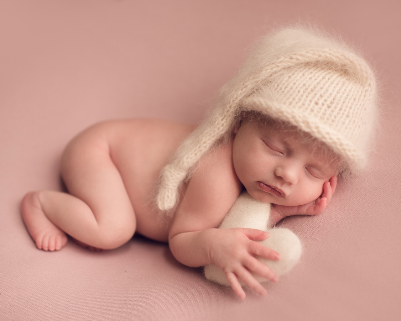 Маленький спящий ребенок в теплой шапке на розовом фоне