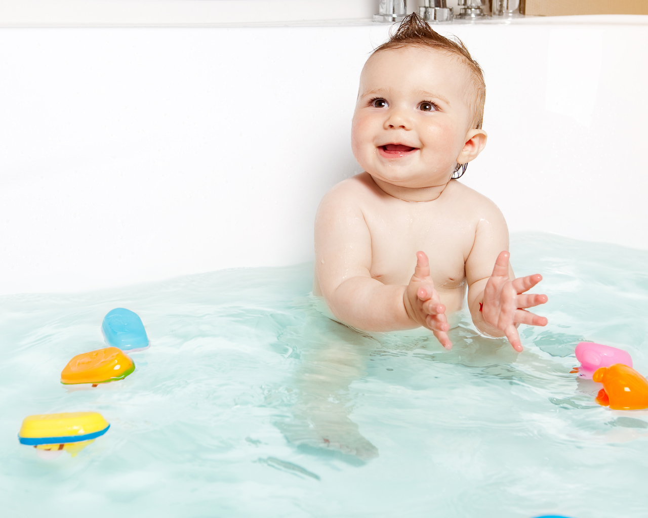 Маленький улыбающийся ребенок с игрушками в ванной 