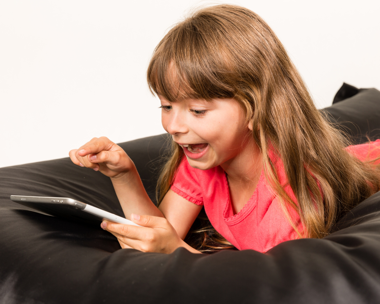 Маленькая улыбающаяся девочка лежит с планшетом