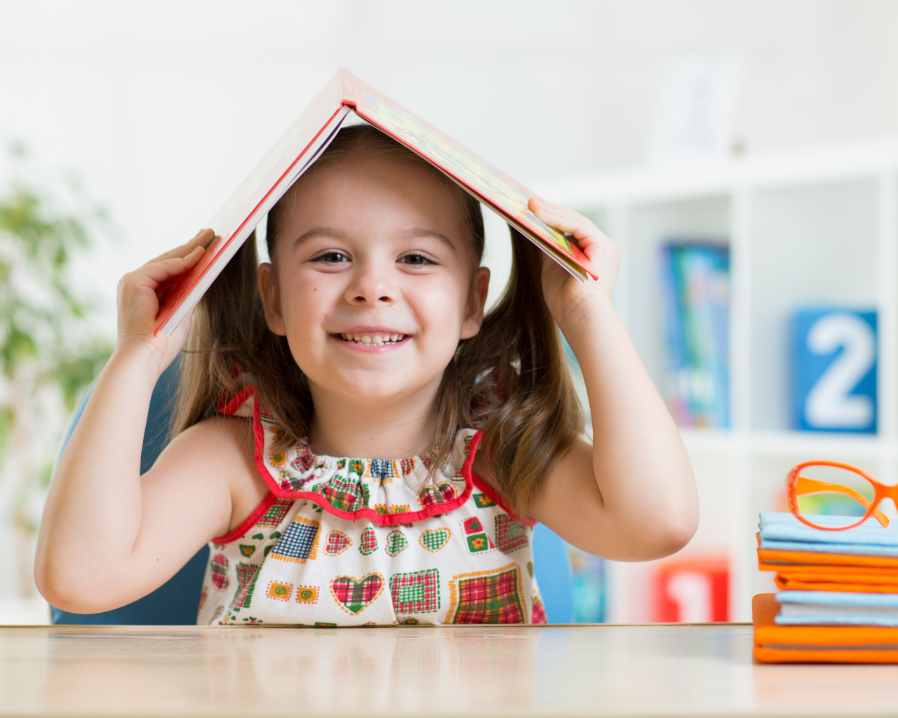 Маленькая улыбающаяся девочка с книгой на голове