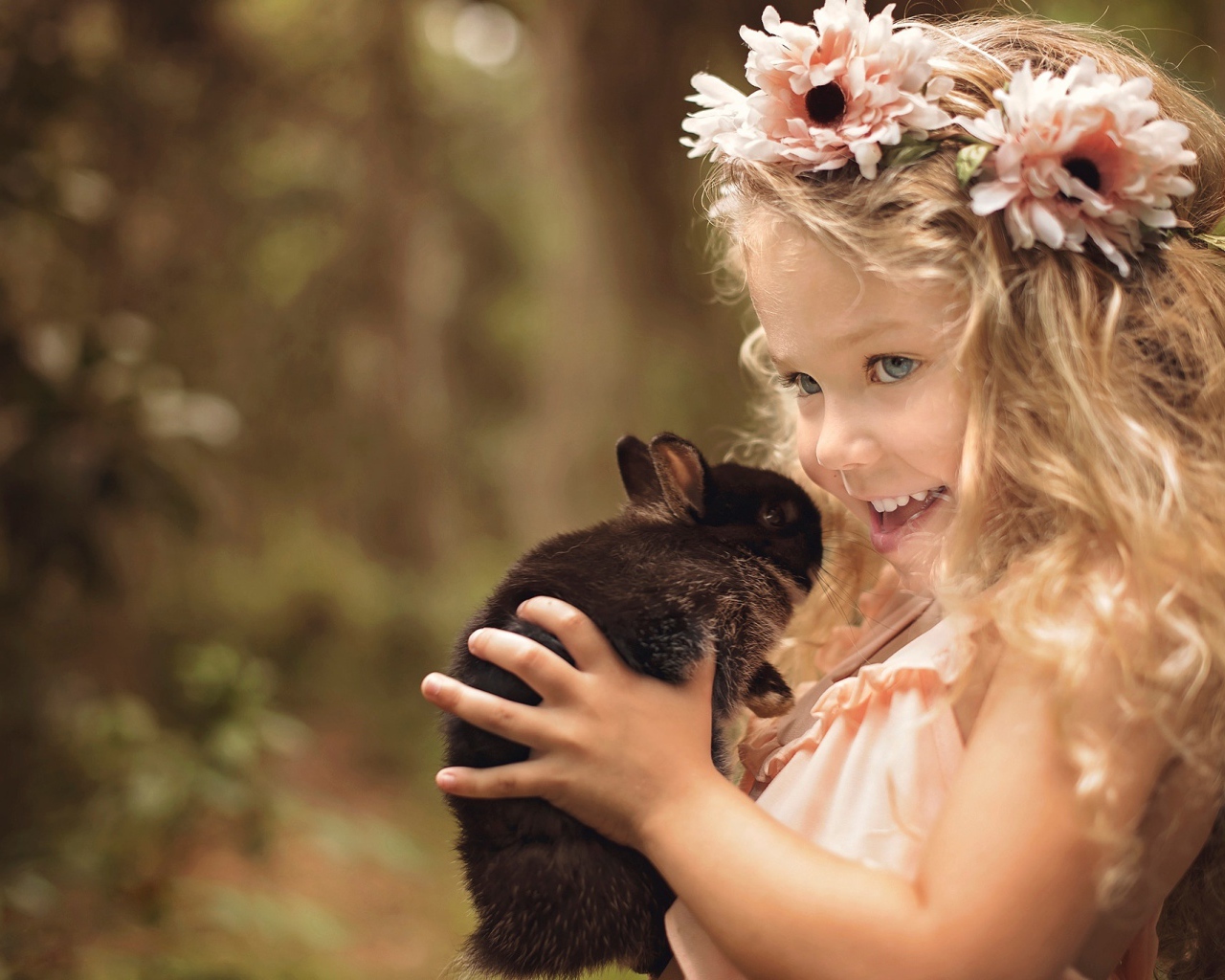 Маленькая улыбающаяся девочка с венком на голове держит кролика