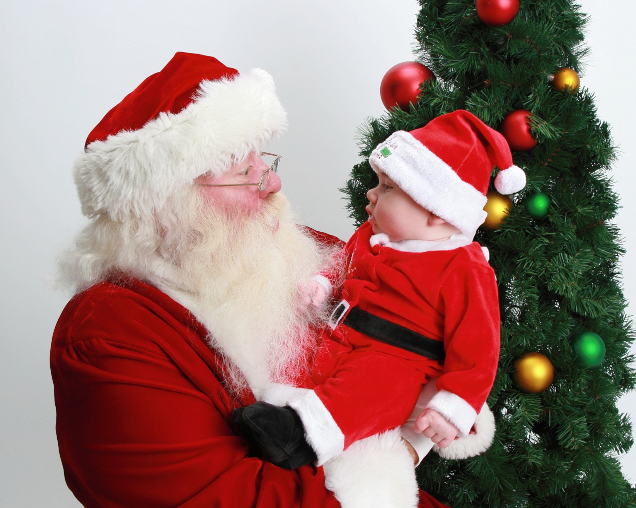 Дед Мороз держит на руках маленького ребенка у елки