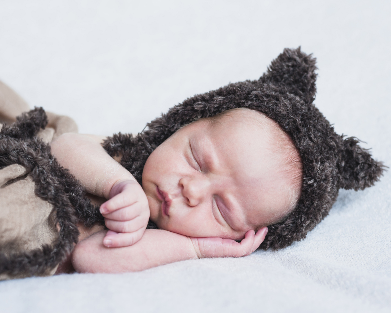 Спящий грудной ребенок в меховой шапке