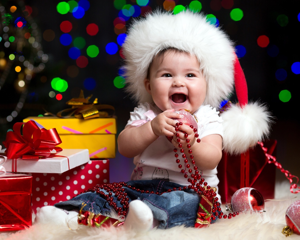 Улыбающийся малыш в новогодней шапке с подарками у елки