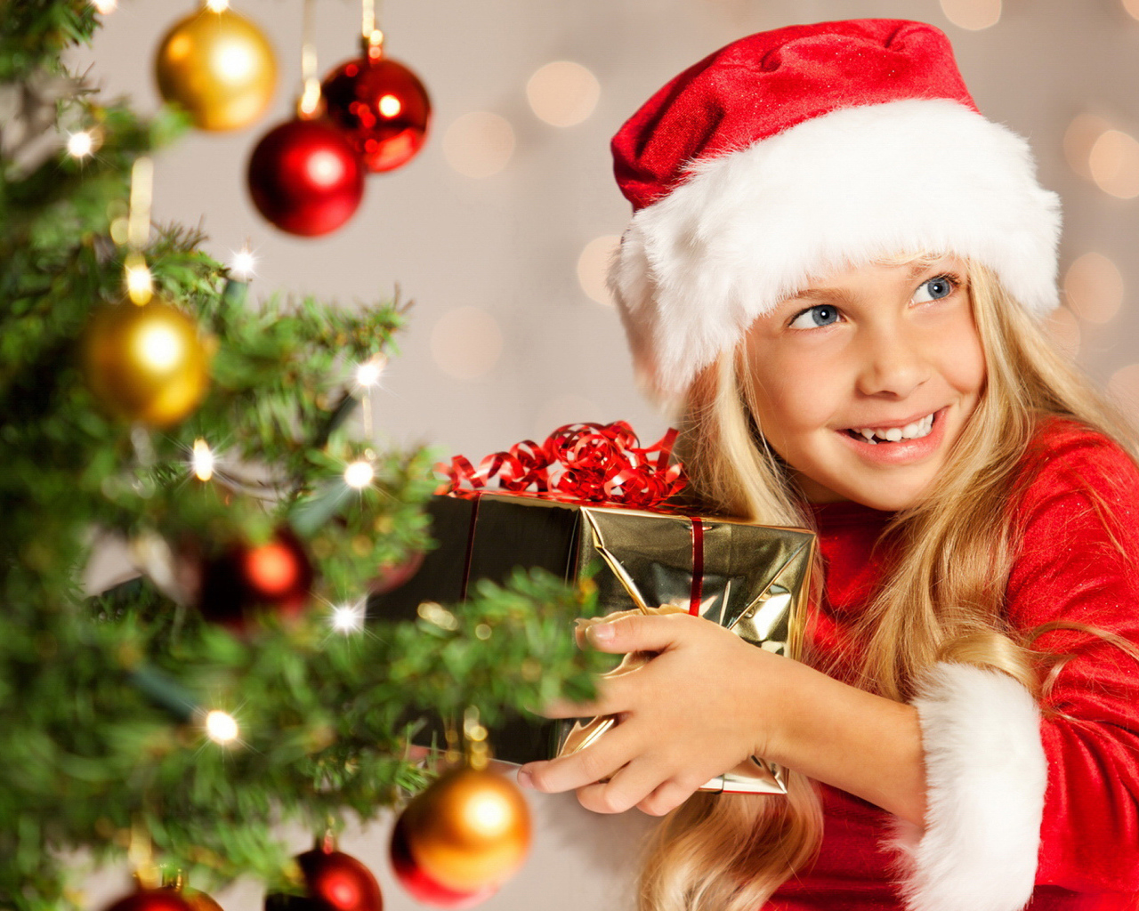 Улыбающаяся девочка блондинка с подарком у елки на новый год 