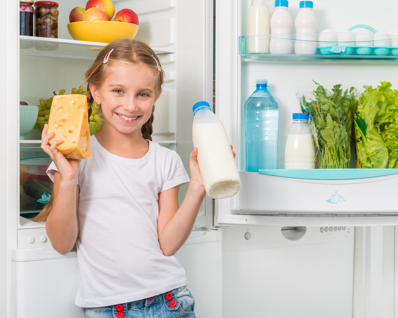Улыбающаяся девочка у холодильника с сыром и молоком