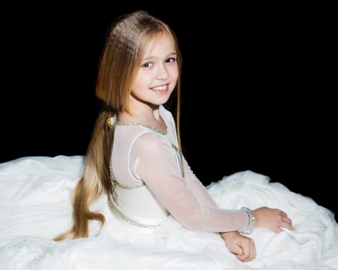 Улыбающаяся девочка в красивом белом платье на черном фоне