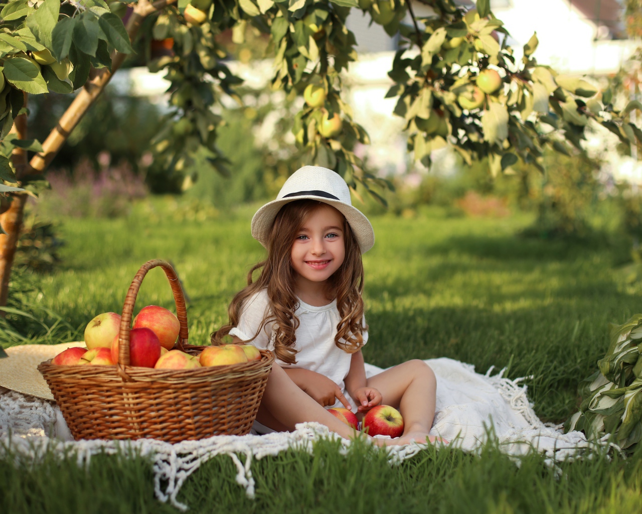 Улыбающаяся девочка сидит на зеленой траве с яблоками