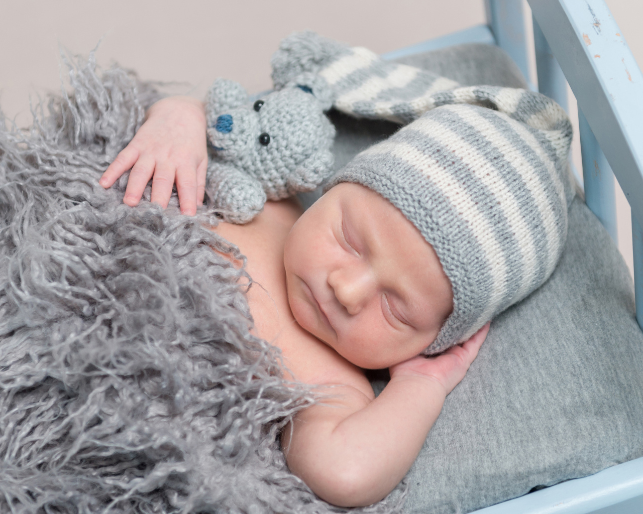 Младенец в вязаной шапке спит с игрушкой под меховым одеялом