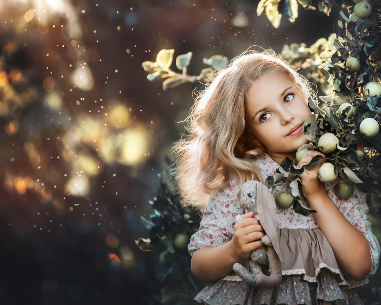 Маленькая девочка стоит у ветки с яблоками