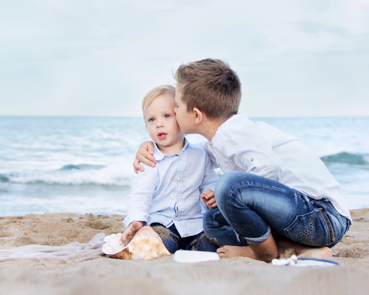 Два маленьких брата сидят на песке на пляже