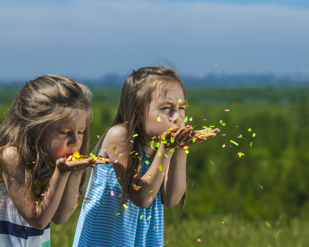Две маленькие девочки сдувают конфетти  с рук