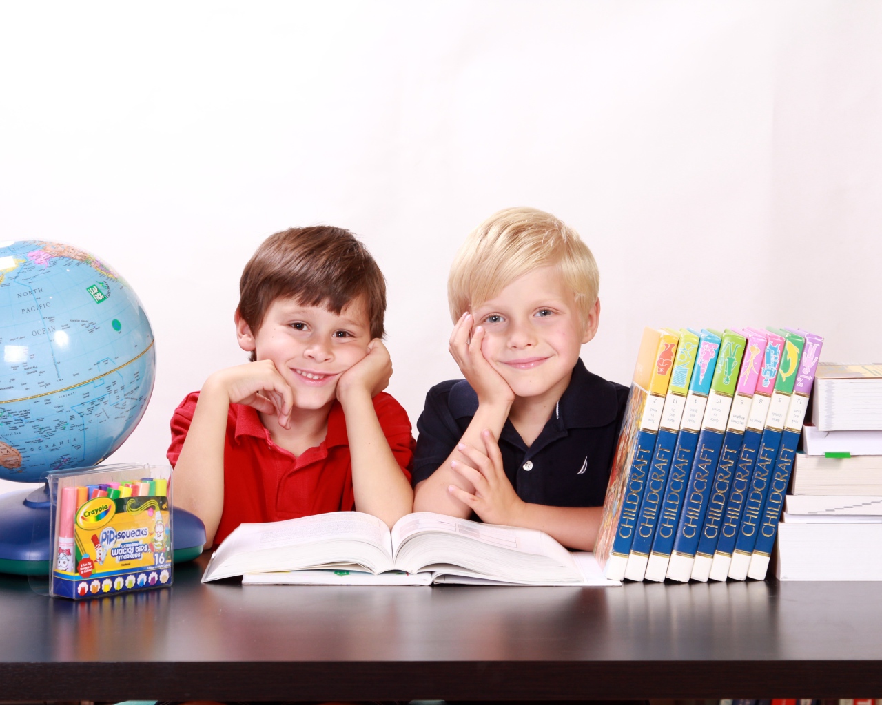 Два маленьких мальчика школьника за столом с книгами и глобусом