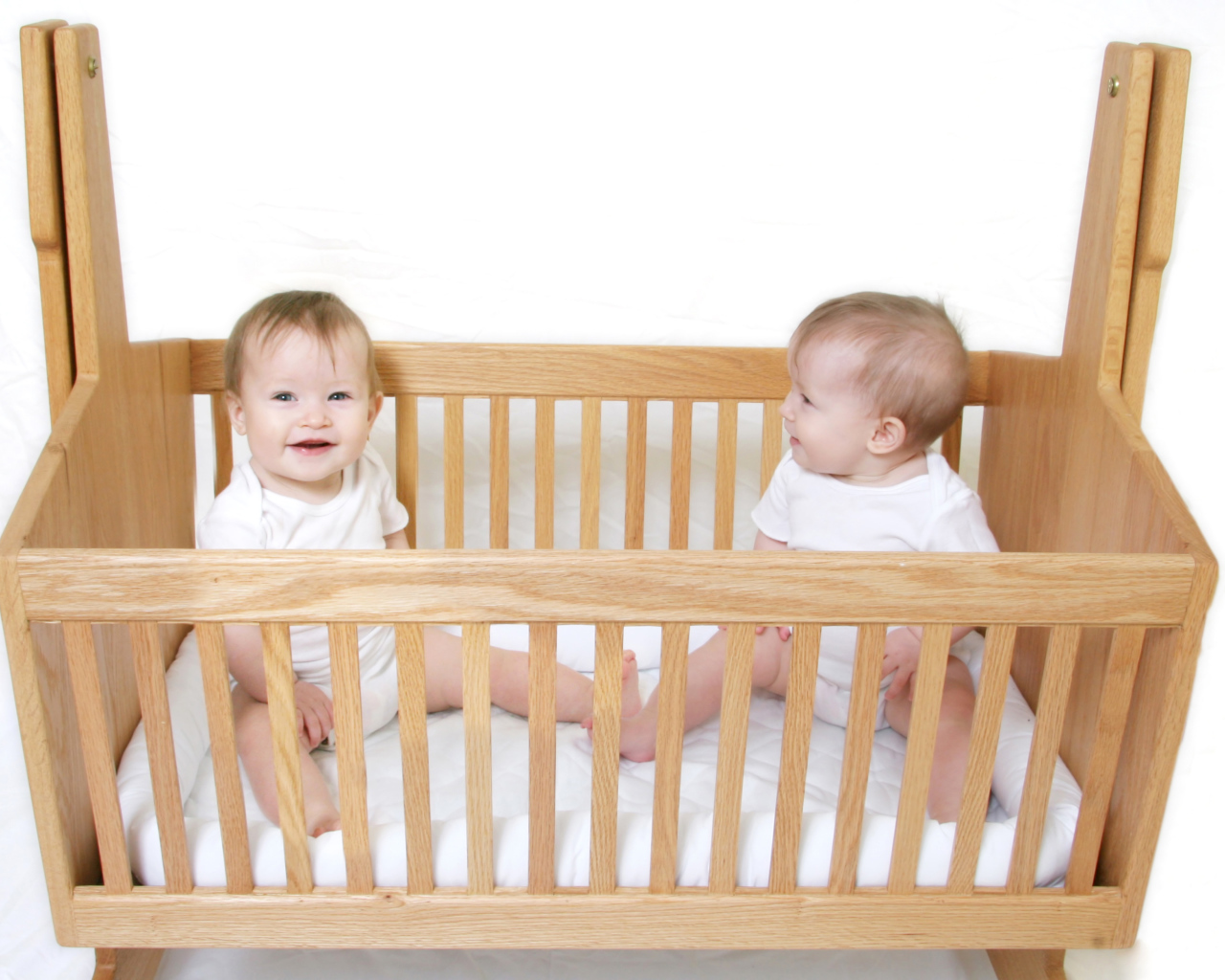 Два улыбающихся малыша в деревянной кроватке