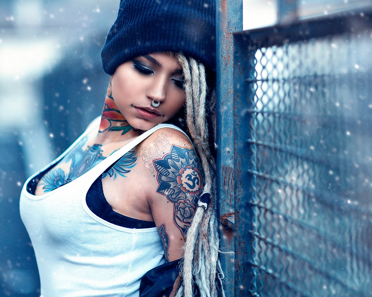 Девушка с татуировками на шее и пирсингом в носу у забора