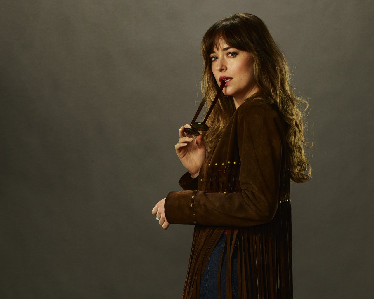 Актриса Дакота Джонсон с очками в руке на сером фоне