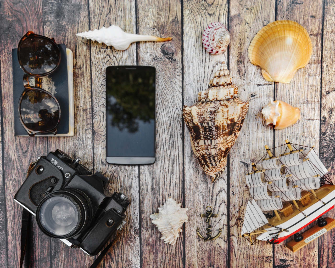 Фотоаппарат, смартфон, ракушки, очки и паспорт на столе