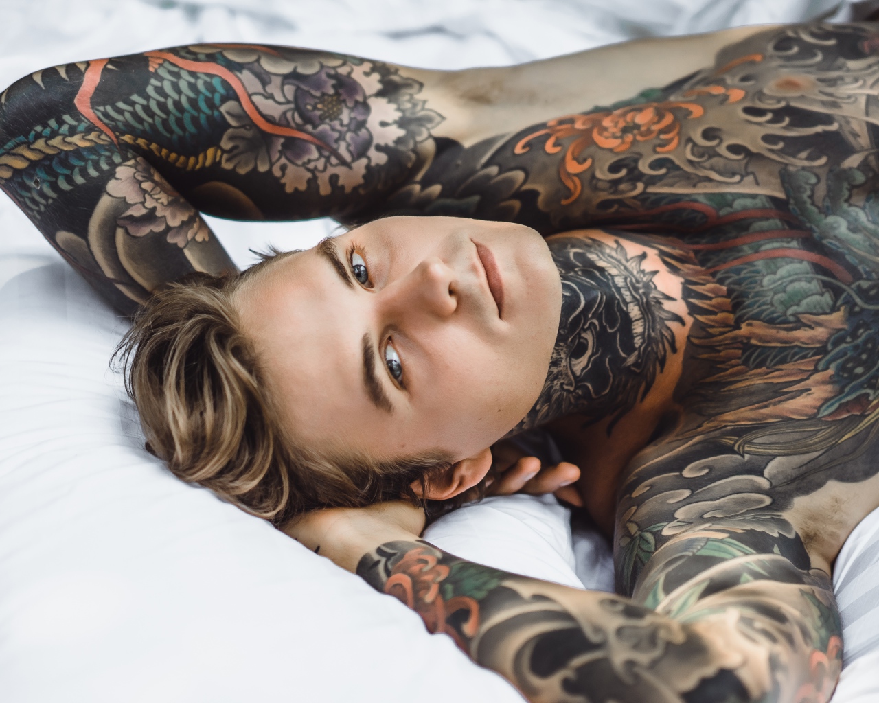 Красивый молодой человек с татуировками на теле лежит на кровати