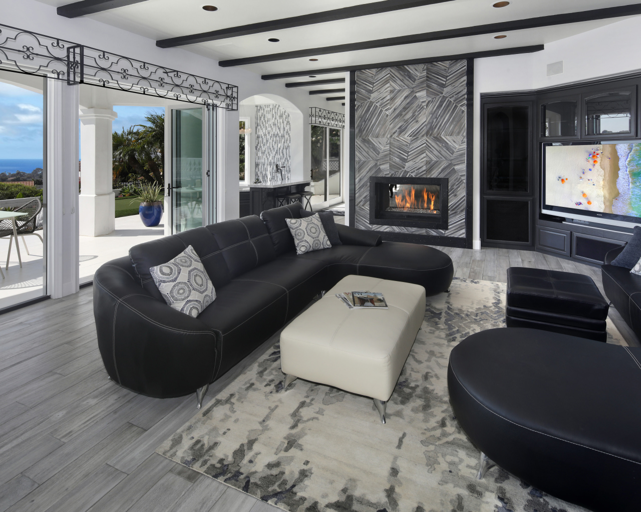 Большая просторная гостиная с черными кожаными диванами, телевизором и камином 