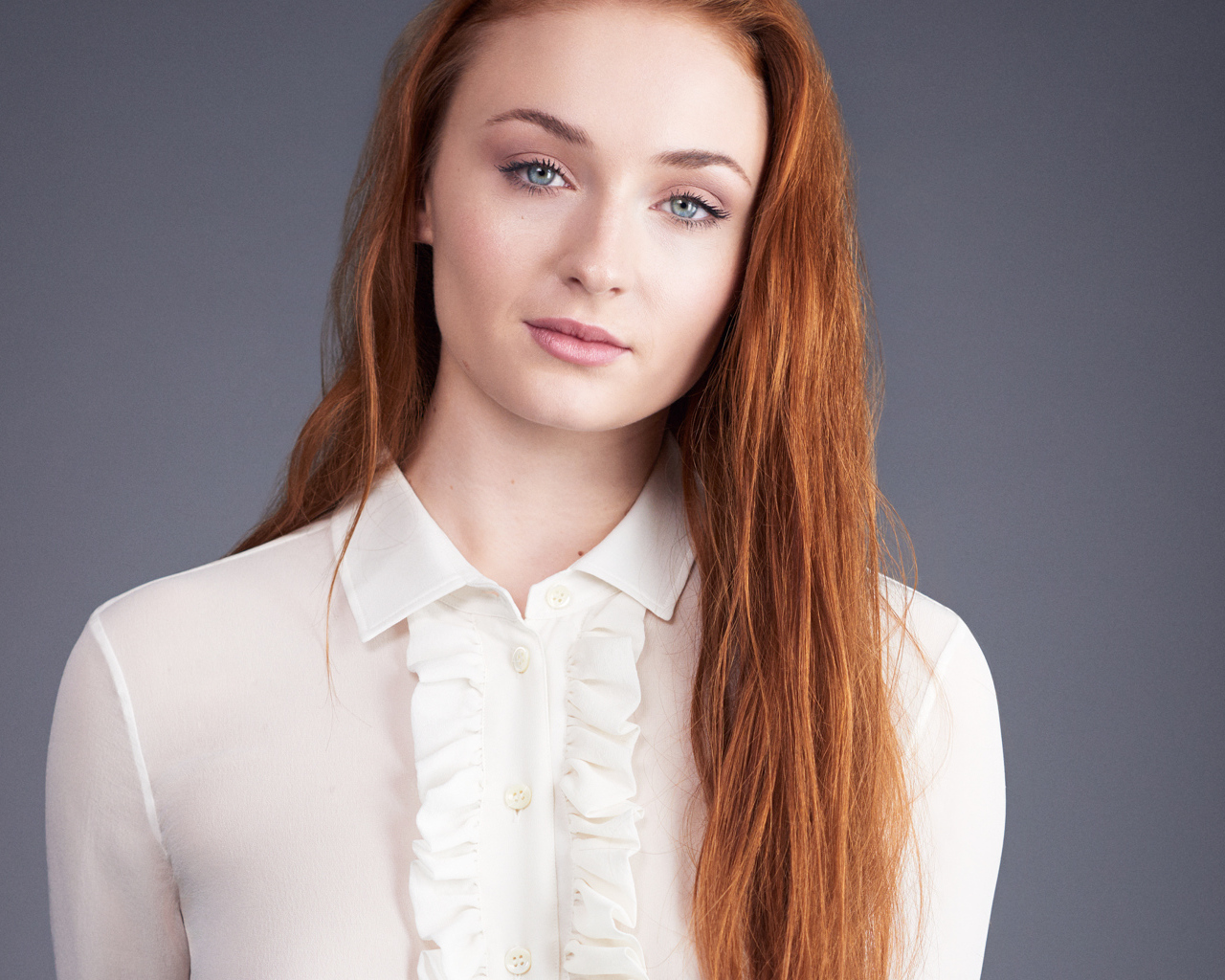 Рыжеволосая голубоглазая актриса Софи Тёрнер на сером фоне
