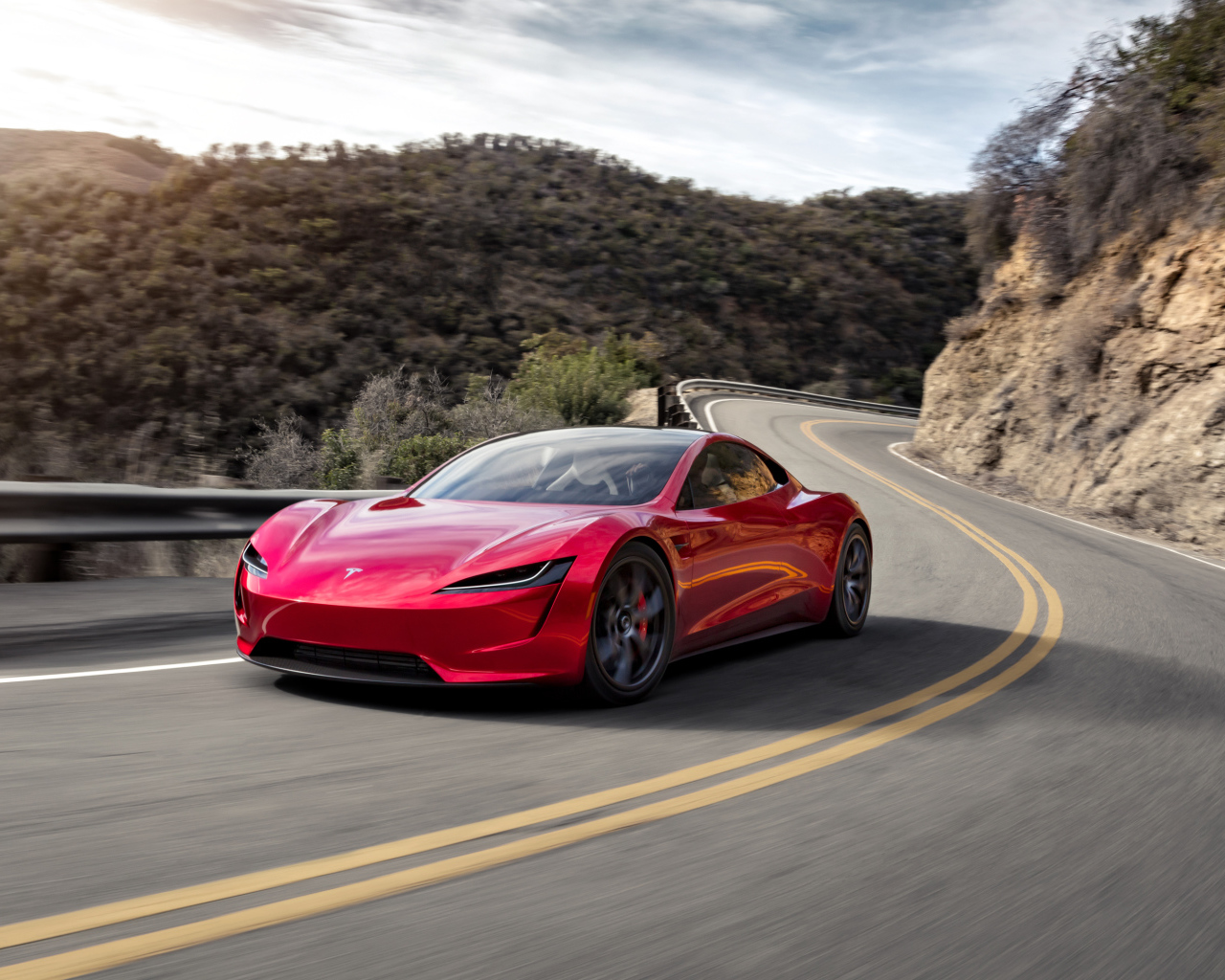 Красный автомобиль Tesla Roadster на трассе у гор 