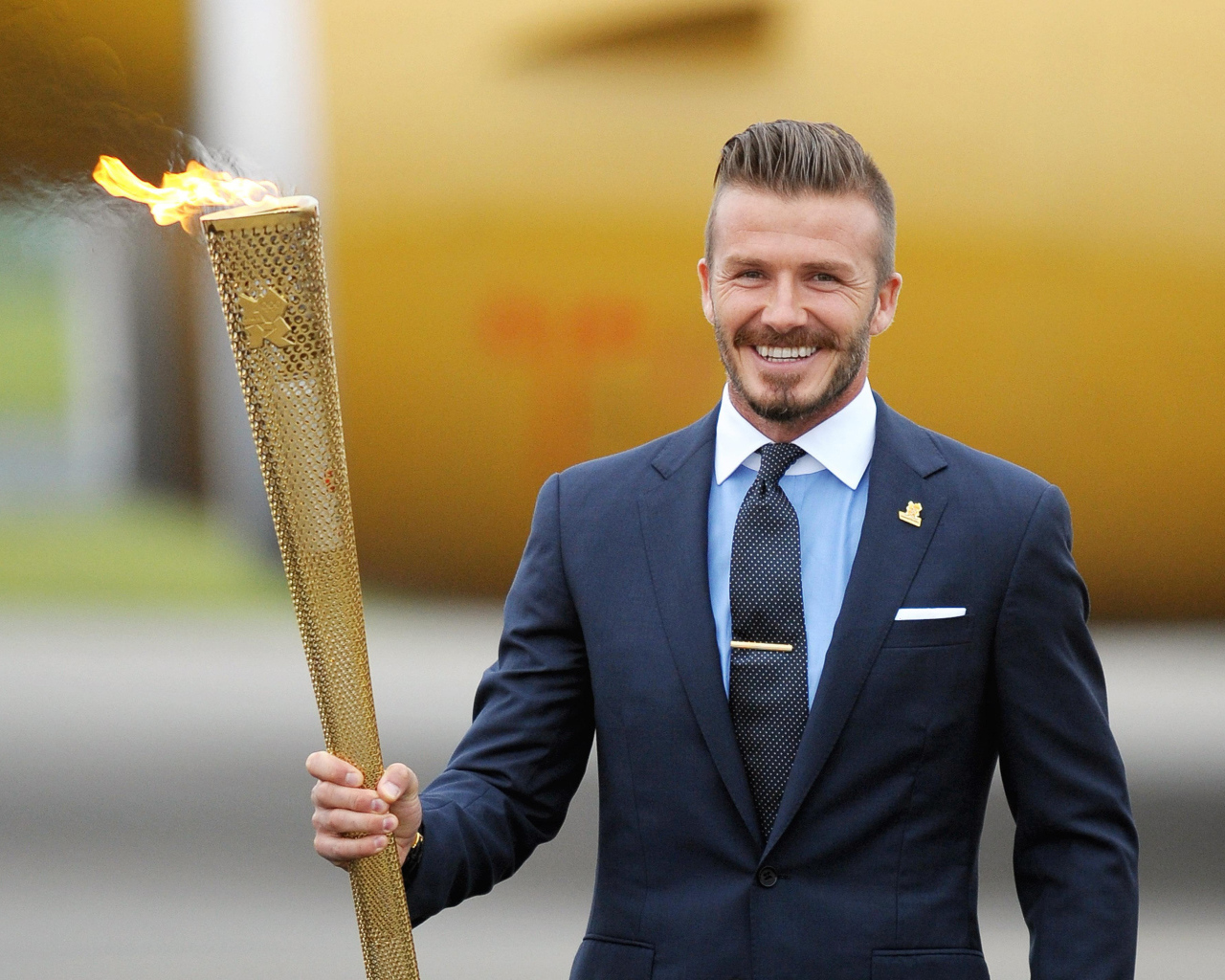 Улыбающийся футболист Дэвид Бекхэм с олимпийский огнем в руке