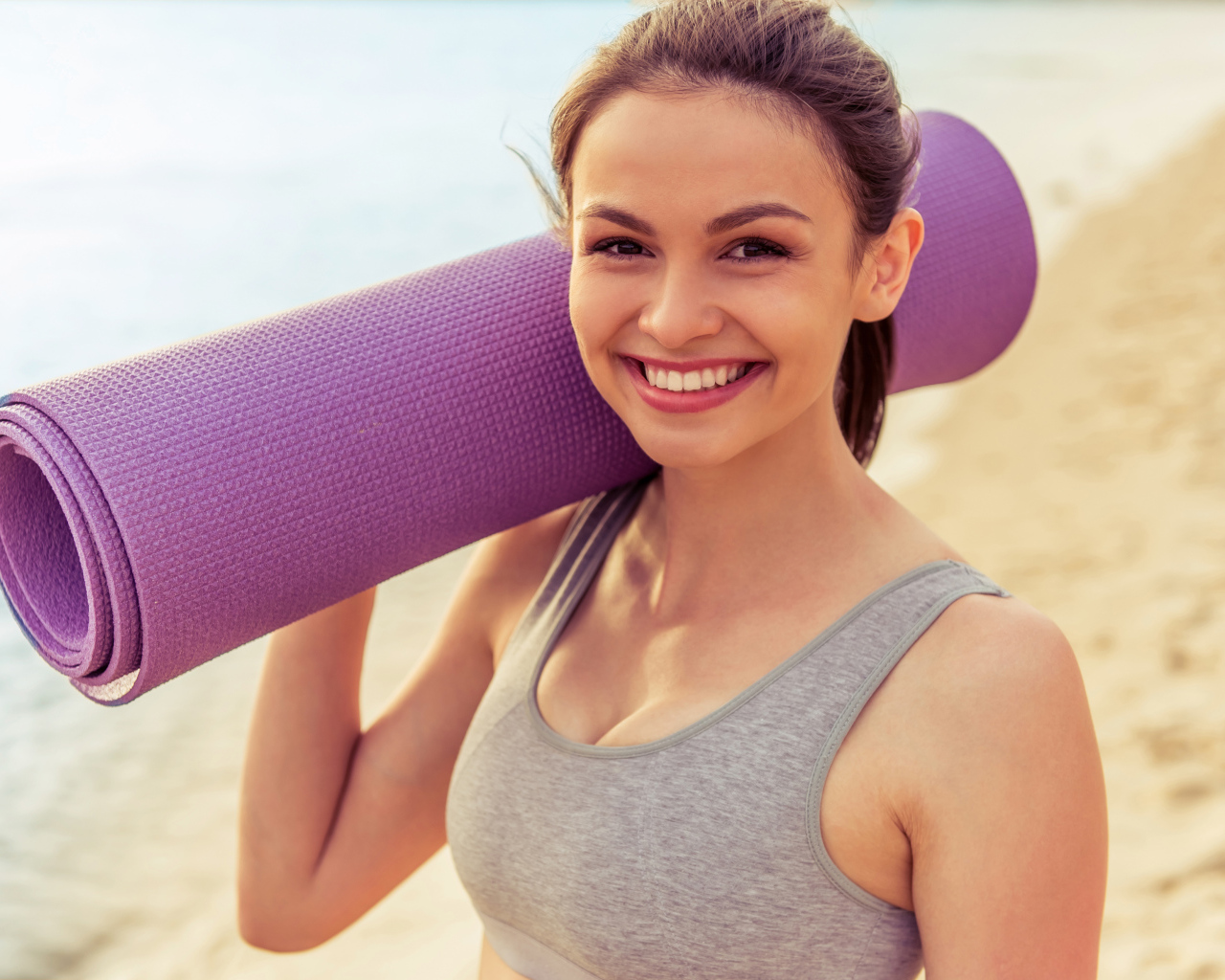 Спортивная девушка с ковриком для йоги на пляже